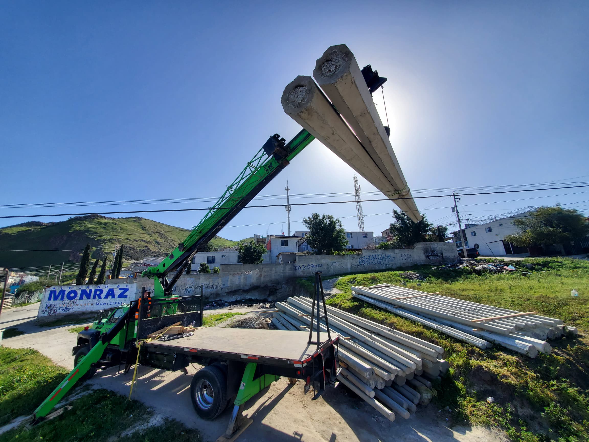 Grúa sobre camión manipulando postes de concreto en obra urbana en Tijuana